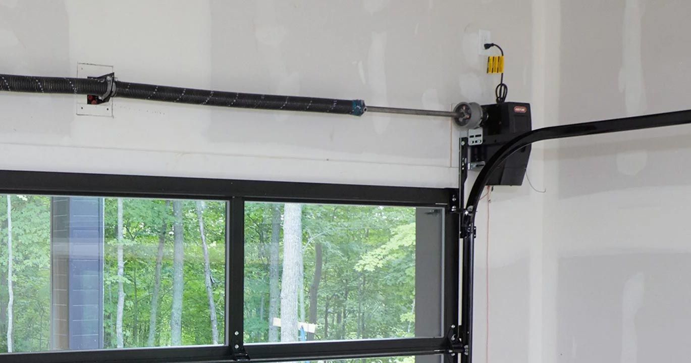 A wall-mounted residential garage door opener installed next to a window with a glass-paneled garage door.