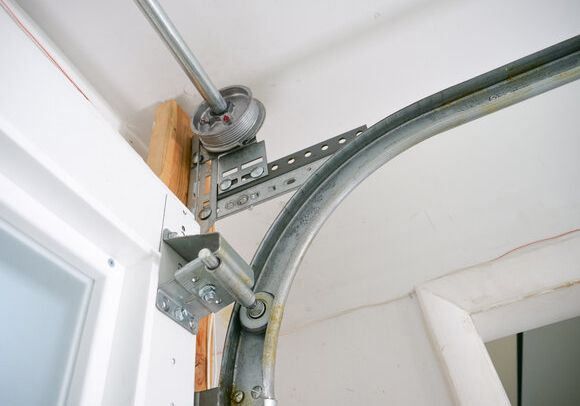 A close-up of a garage door track and roller assembly mounted to a wooden header and wall.