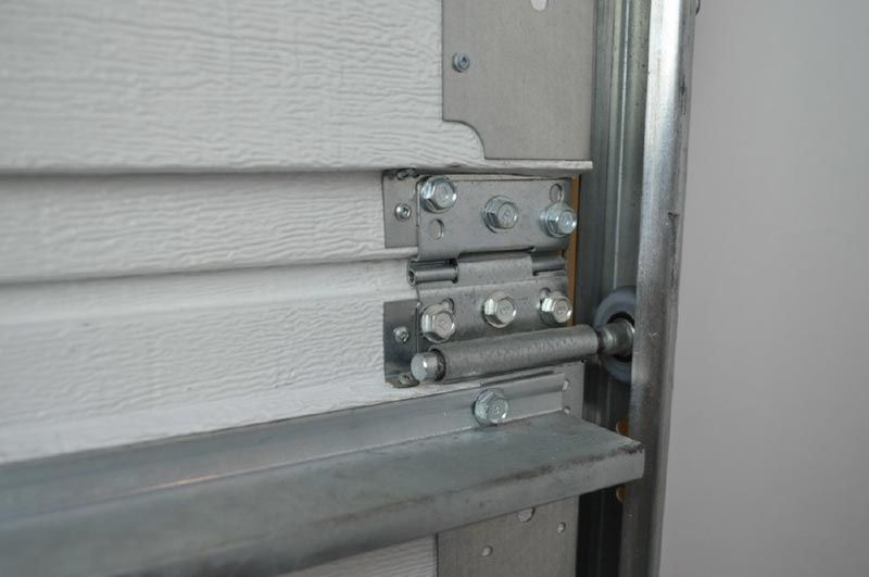 Metal hinge and roller mechanism on the interior side of a white garage door panel.