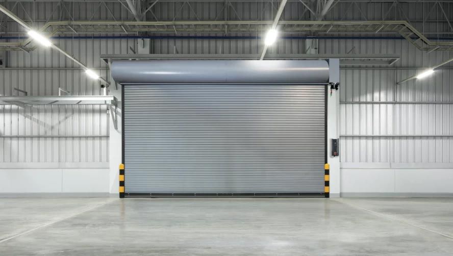 A large, closed grey industrial roll-up door in a well-lit warehouse with concrete flooring.