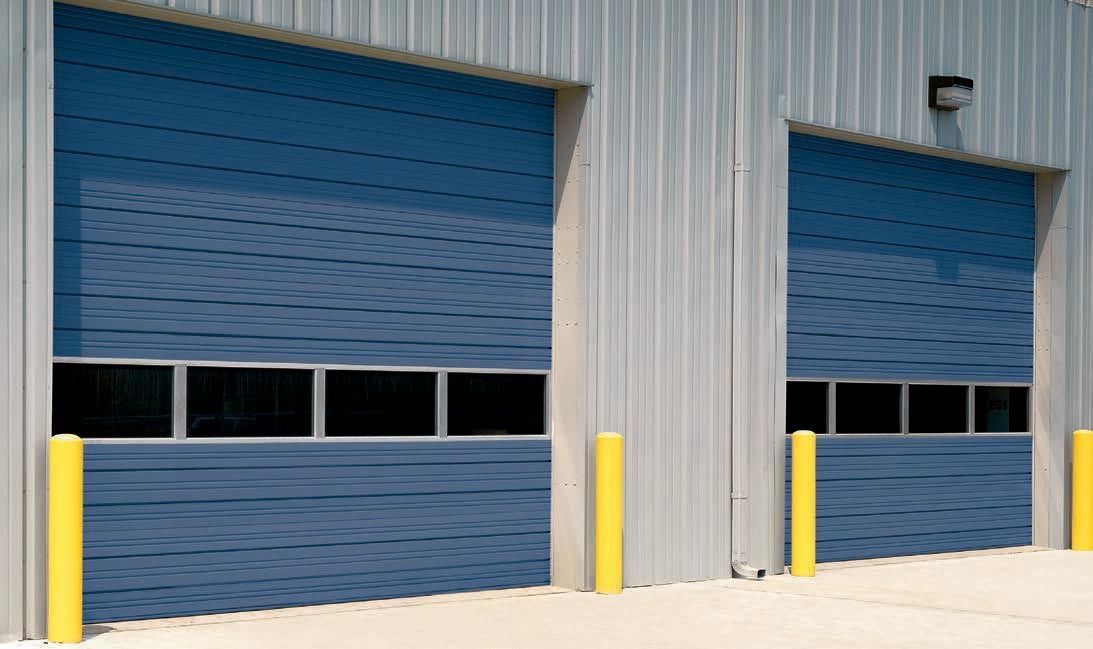 Two blue industrial garage doors with window panels, flanked by yellow safety bollards on a concrete exterior.