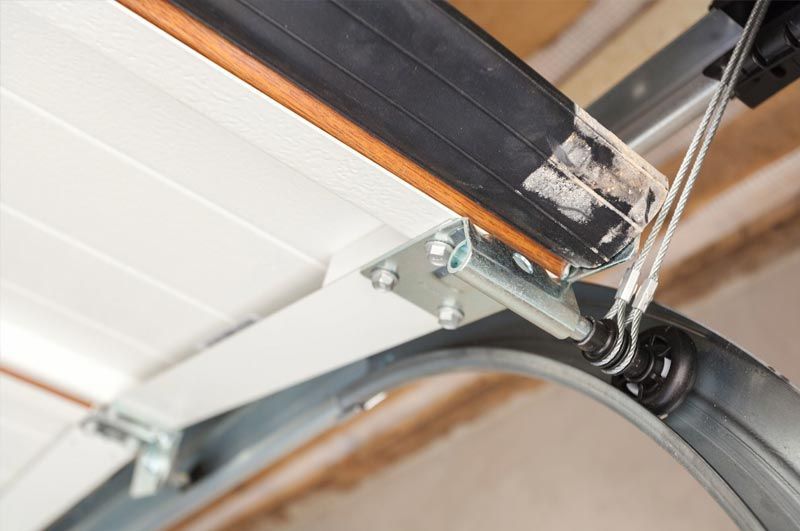A close-up view of a metal garage door bracket and roller assembly with a steel cable attached to a track.