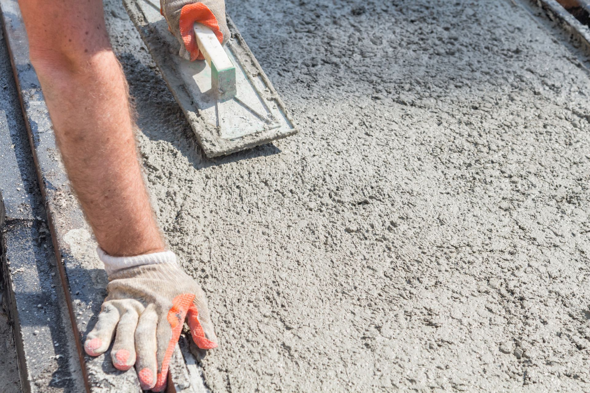 A man is spreading concrete on a sidewalk with a trowel.