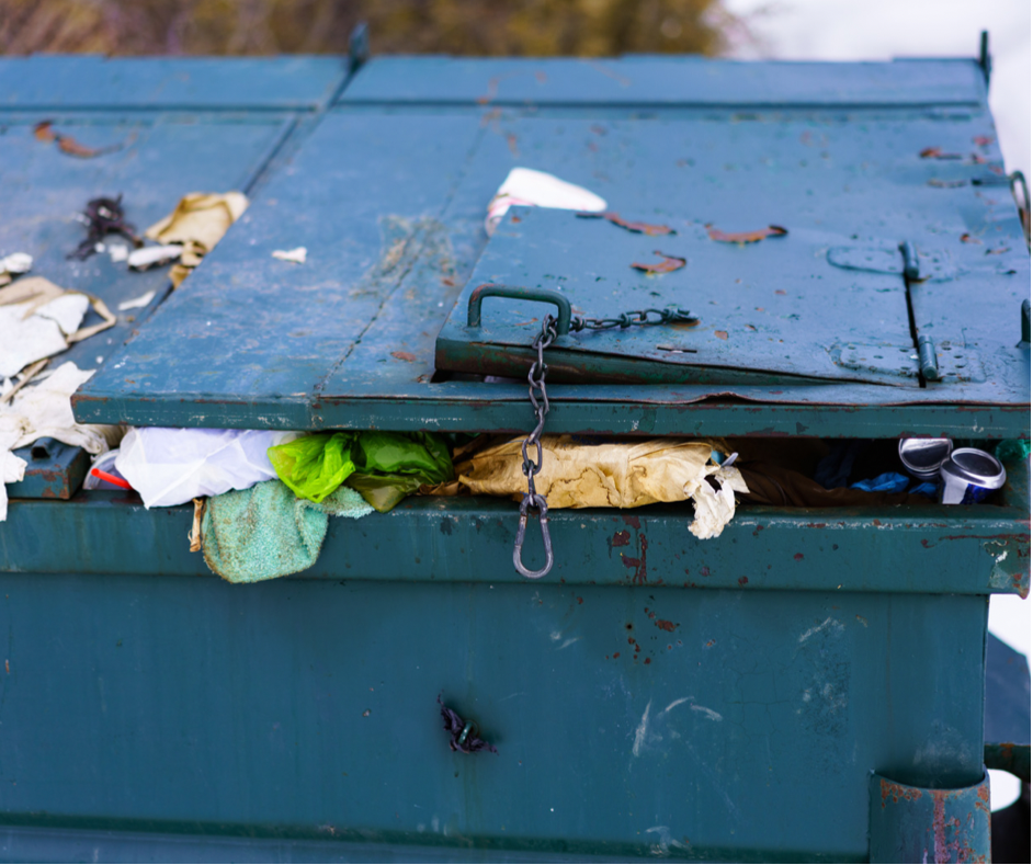 blue garbage dumpster with lid that can't close because it has been overfilled with garbage