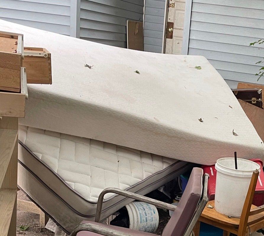 2 mattresses surrounded by a pile of junk behind a blue house