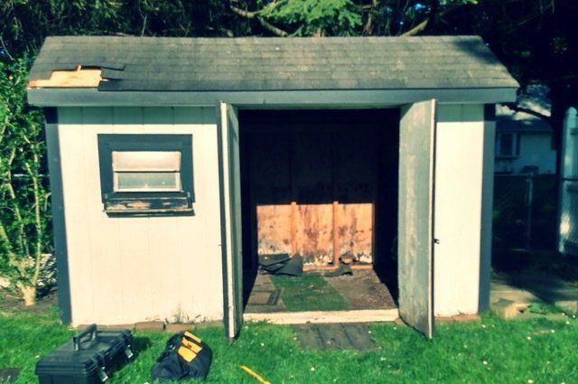 a white shed with open doors that is missing a few shingles
