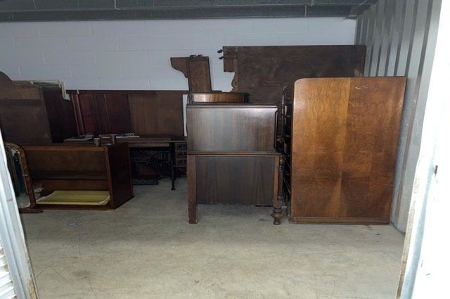 wooden furniture and dressers inside of white storage unit with clean concrete floor