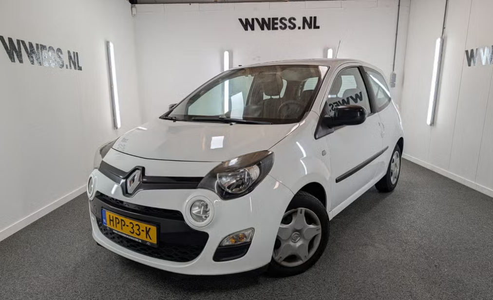 Een witte compacte auto staat tentoongesteld in een showroom met een tegelvloer en het WWESS.NL-logo op de muren.