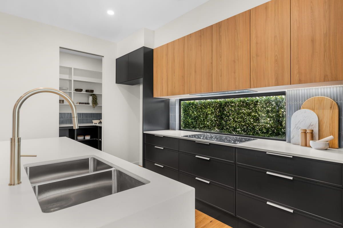 Modern kitchen with black lower cabinets, wood upper cabinets, white island, and stainless sink faucet
