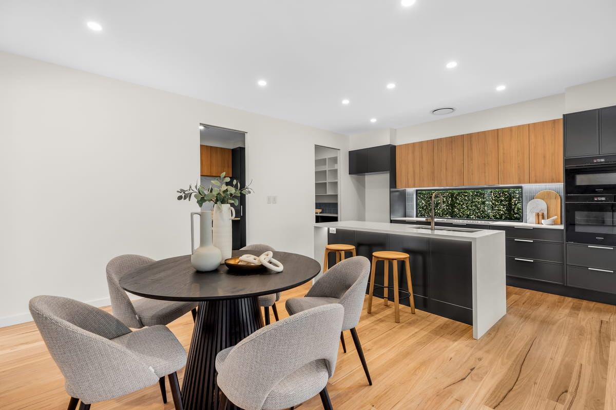 Modern open-plan kitchen and dining area with wood floors, black island, and round table with upholstered chairs