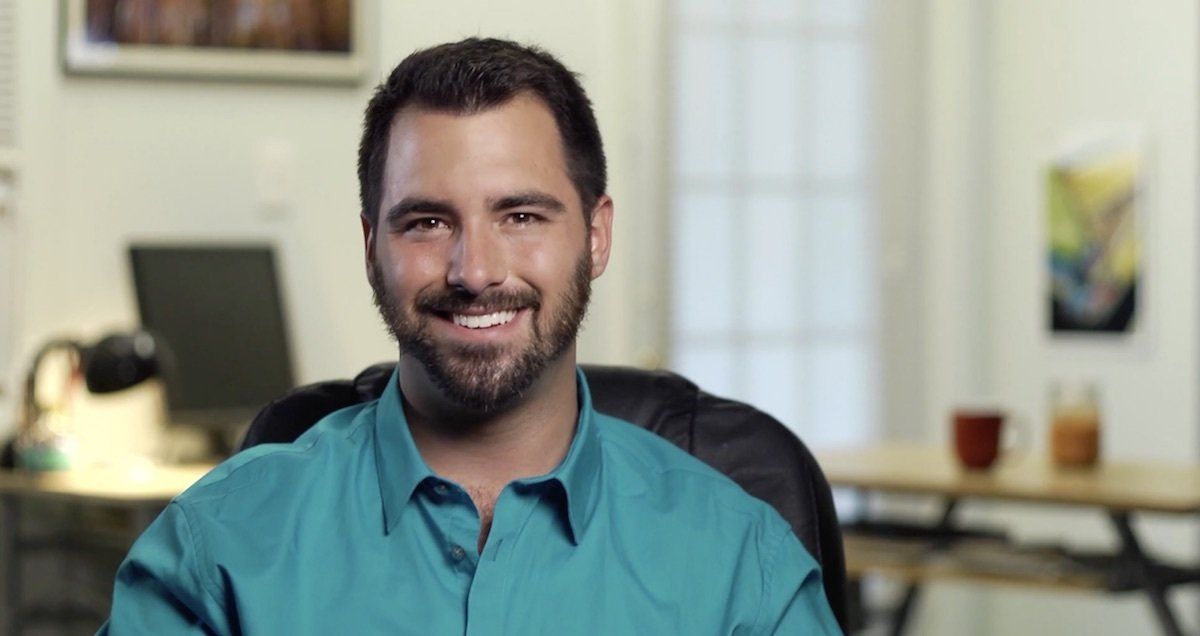 A man with a beard is smiling while sitting in a chair.