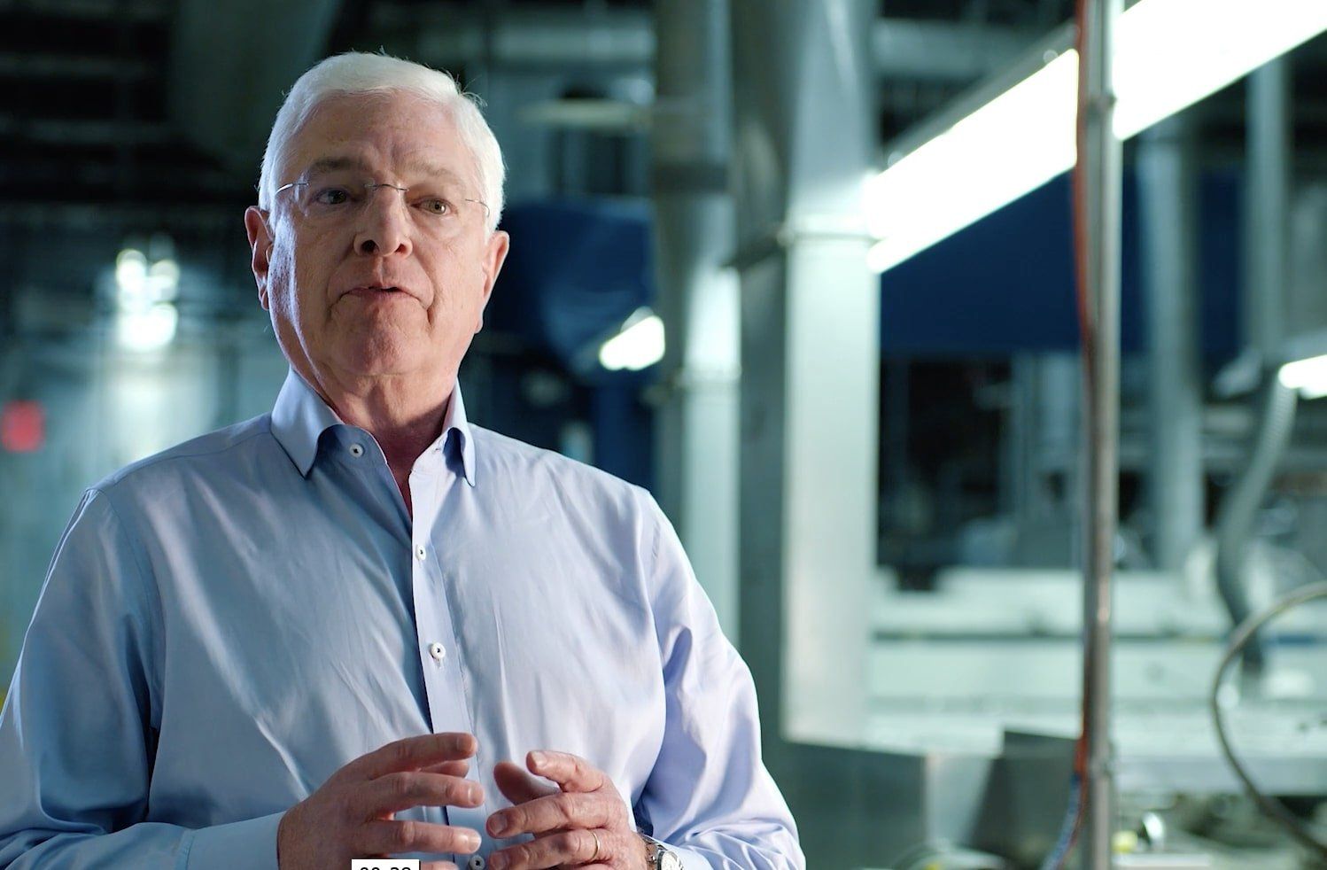 An older man in a blue shirt and glasses is standing in a factory.