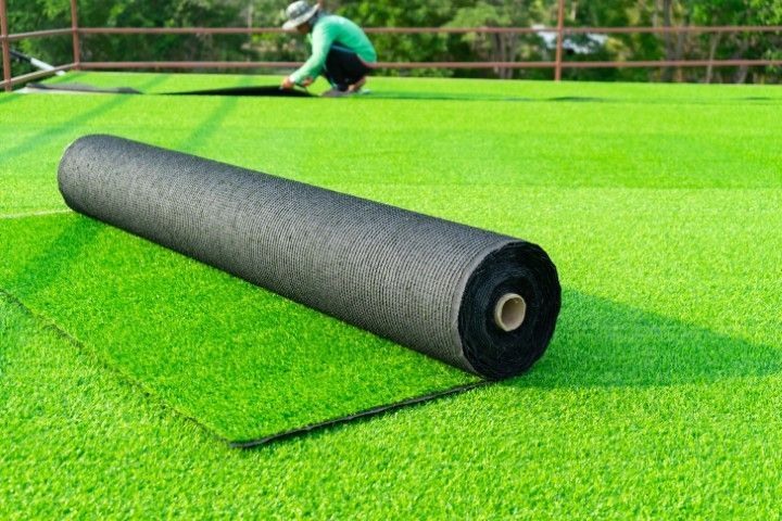 Roll of artificial turf on green grass with a person installing in the background.