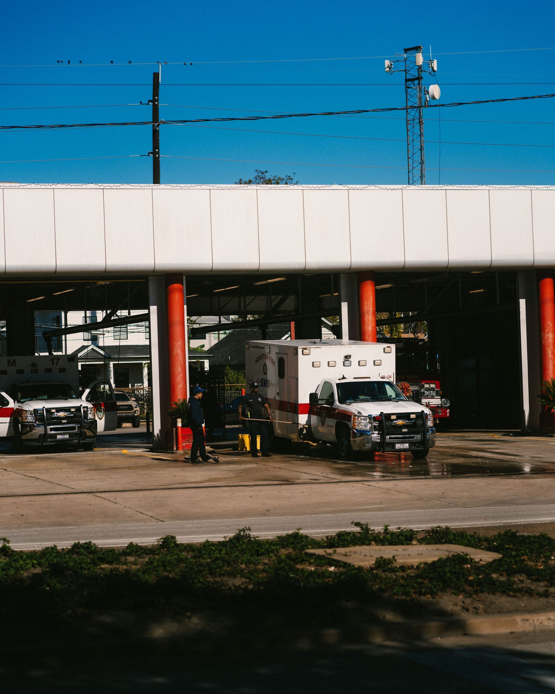 Ambulances and fire trucks parked under a white overhang at a roadside station under a blue sky