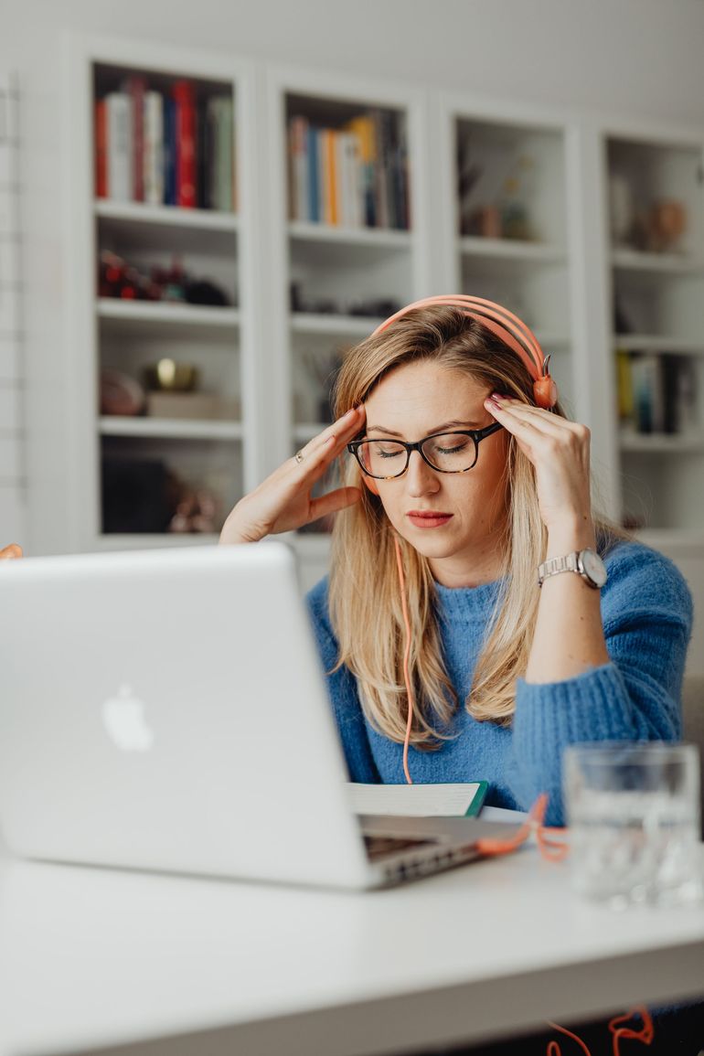 Woman in blue sweater adjusting glasses while working at a laptop in a bright home office