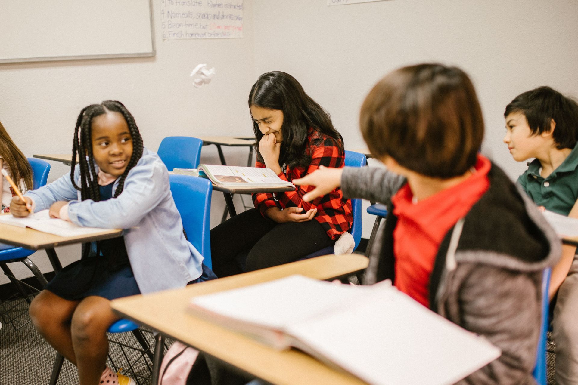 Students in a classroom working together around desks, with notebooks and papers open.