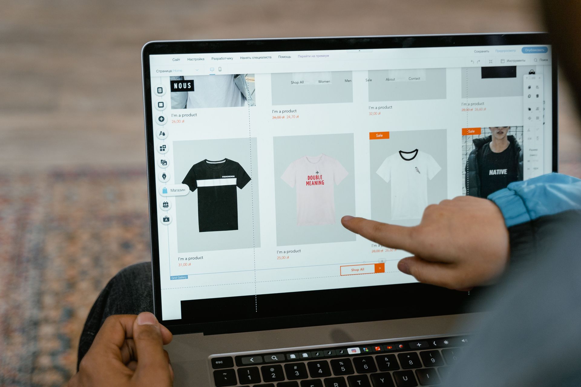 Person pointing at laptop screen showing an online clothing store grid