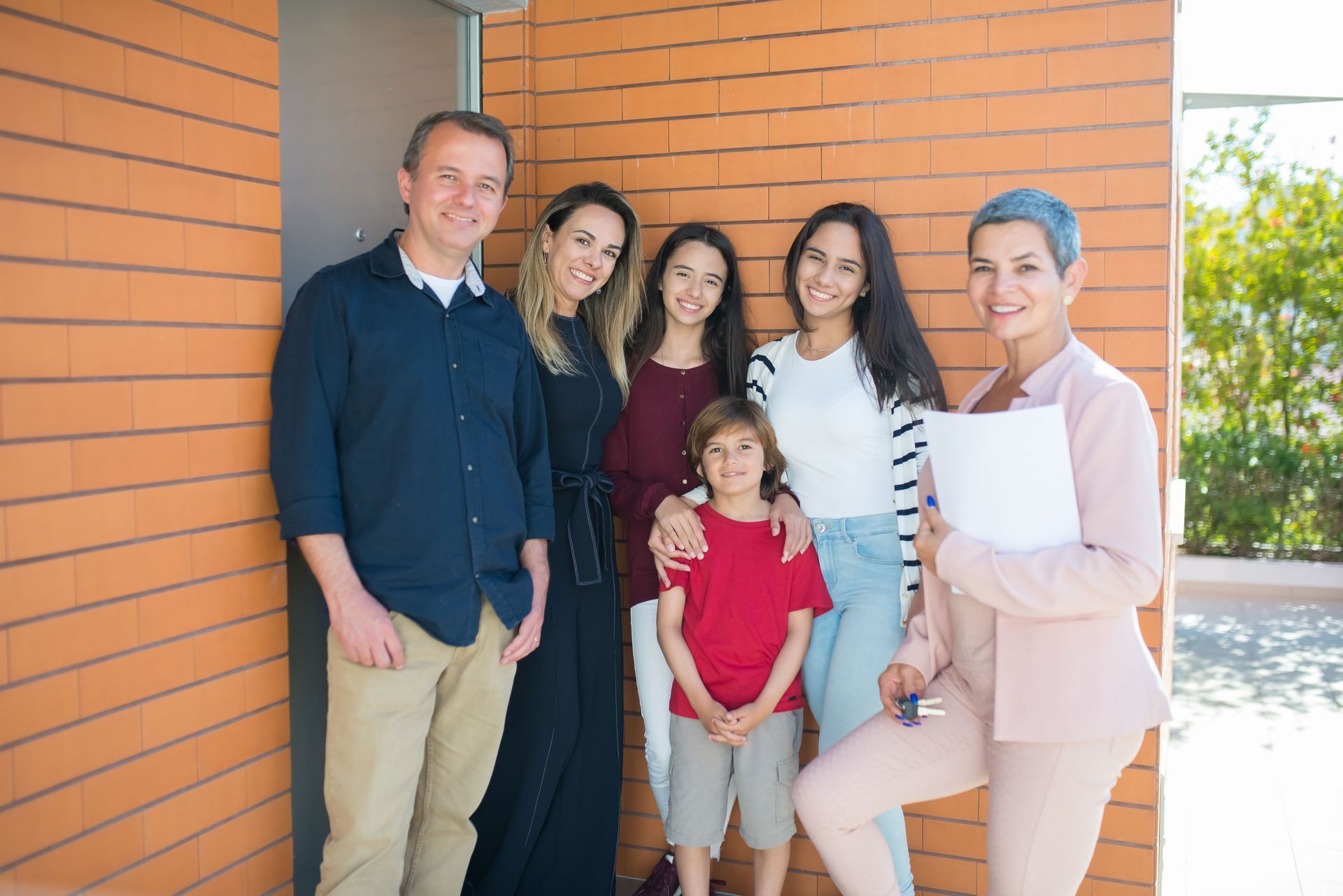 Five people posing together in front of a brick wall, smiling outdoors.