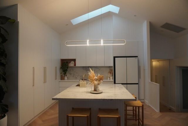 Modern kitchen with island, white cabinets, and skylight. Includes a refrigerator, stools, and pendant lighting.