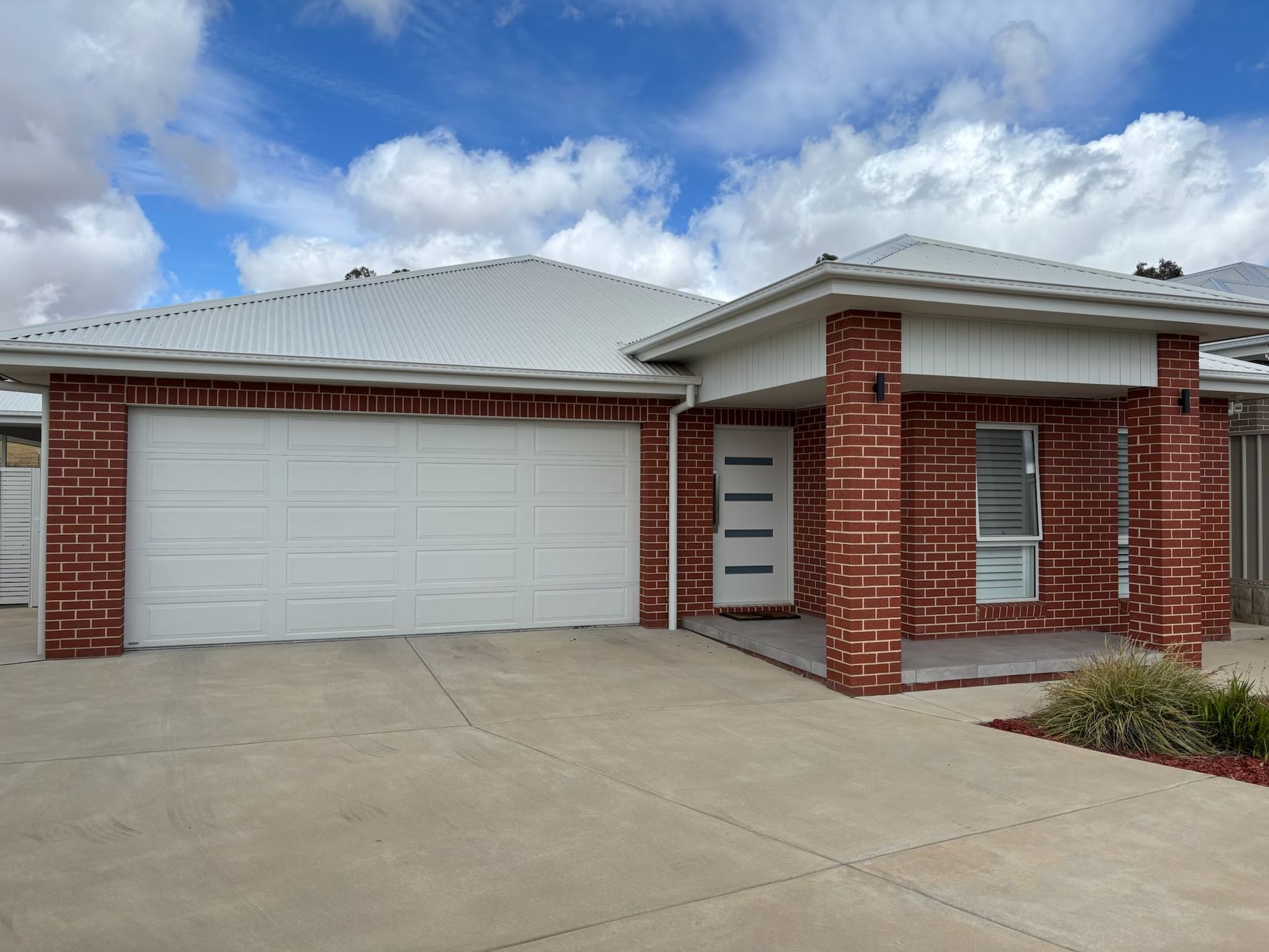 Brick house with white garage door and roof; blue sky. — Hallam & Sons in Beard, ACT