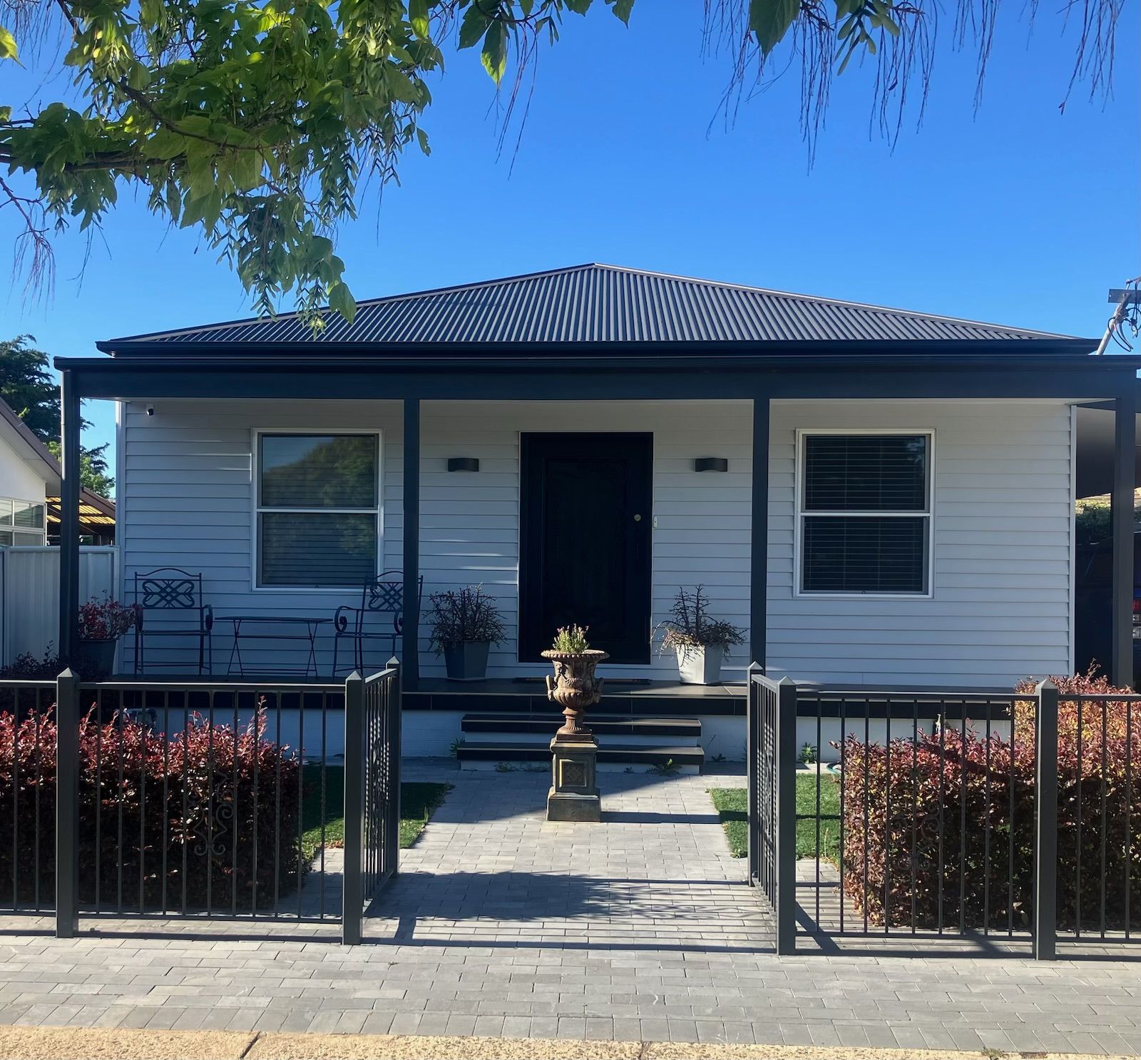Small, light gray house with black trim, porch, and iron fence, on a sunny day. — Hallam & Sons in Beard, ACT