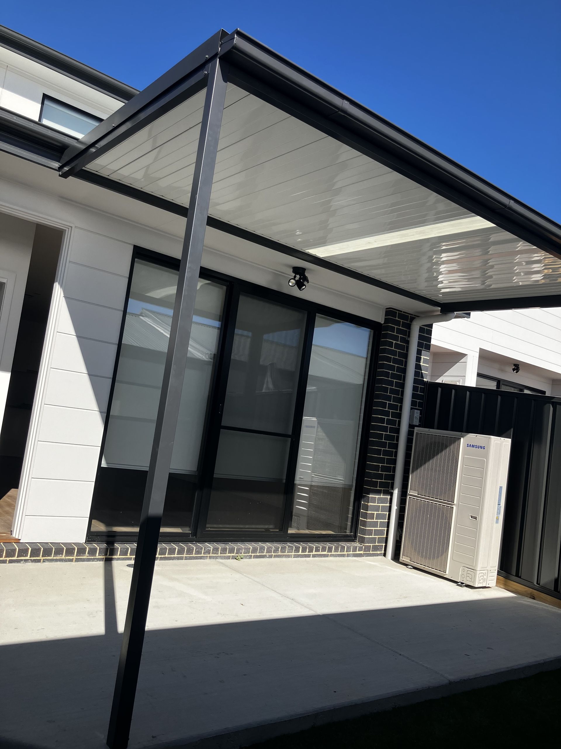 Patio with black and white awning, sliding doors, and air conditioning unit. — Hallam & Sons in Beard, ACT