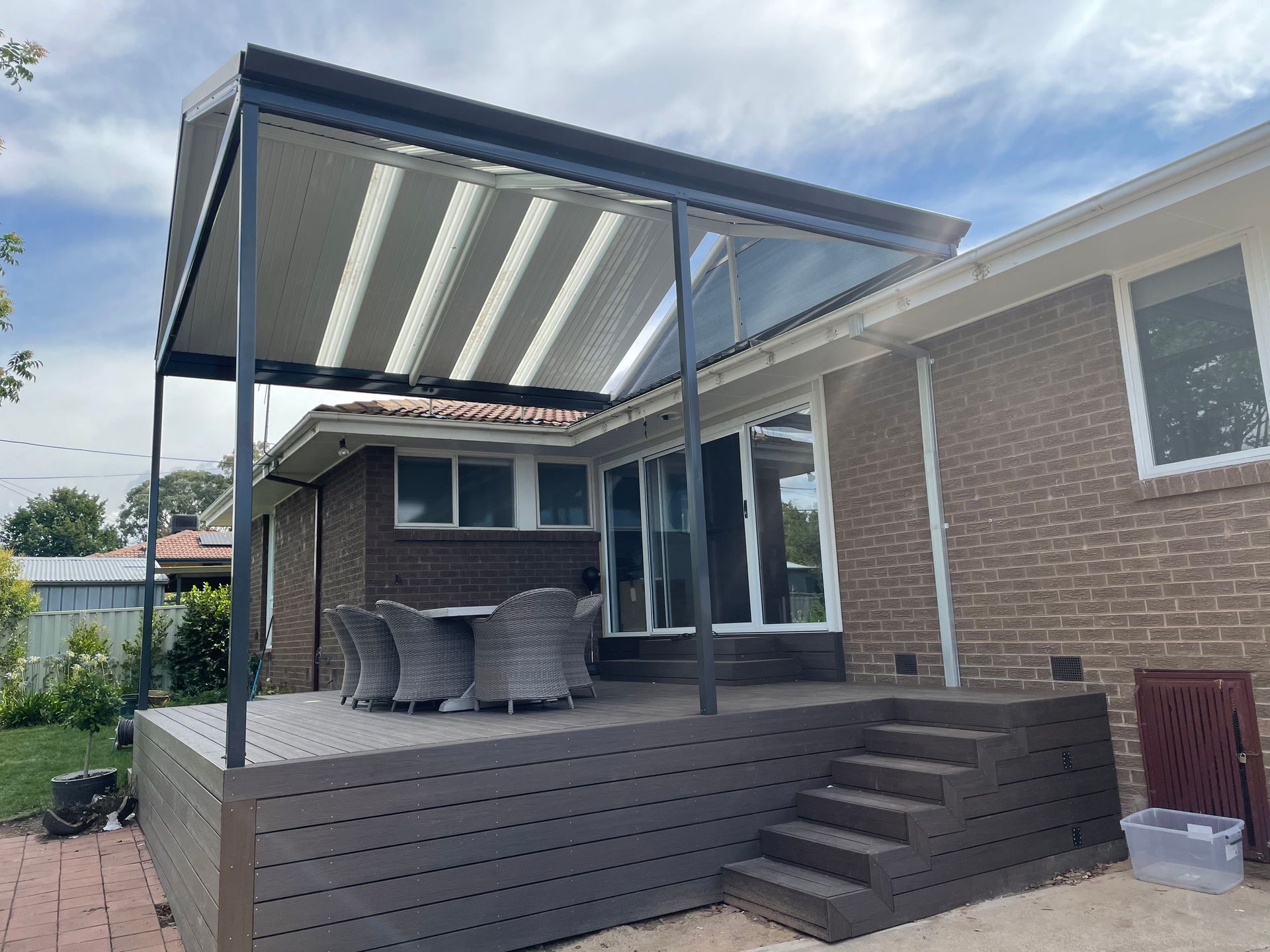 Patio with dark wood deck, brick house, and a pergola with striped roof. — Hallam & Sons in Beard, ACT