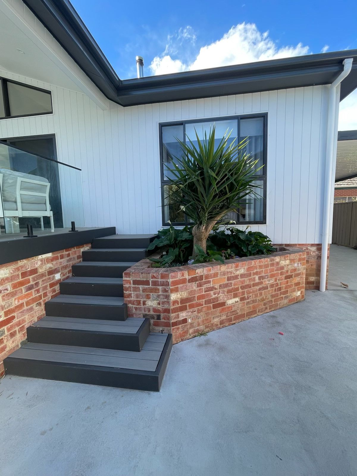 Exterior of a house with steps, brick planter, and a tree. White siding, black trim, and a clear sky. — Hallam & Sons in Beard, ACT