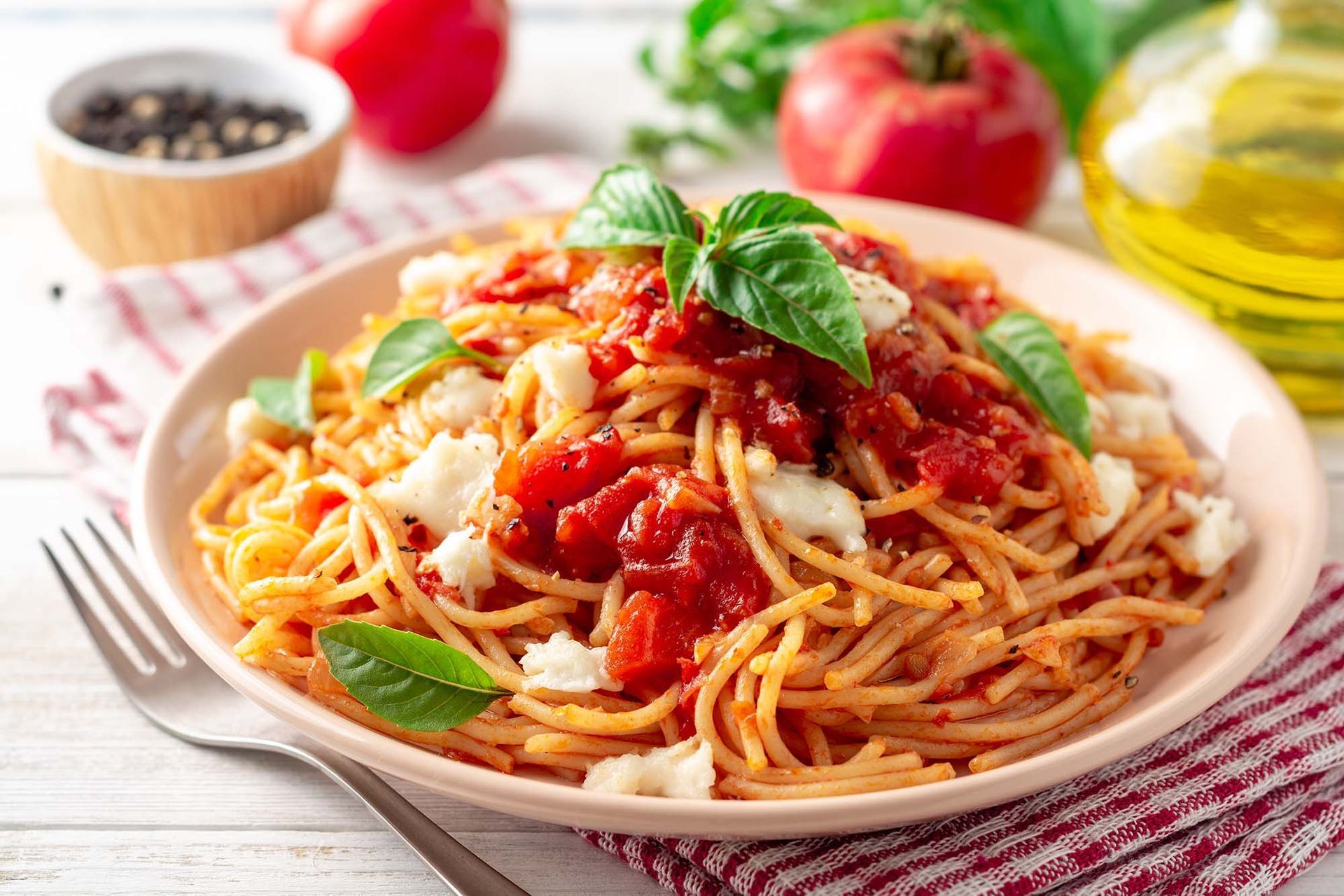 Plate of spaghetti with tomato sauce, basil, and cheese on a table with fresh ingredients nearby
