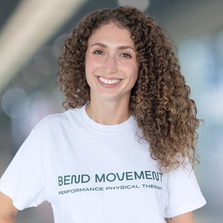 Smiling person in a white Be Up Movement T-shirt against a blurred indoor background