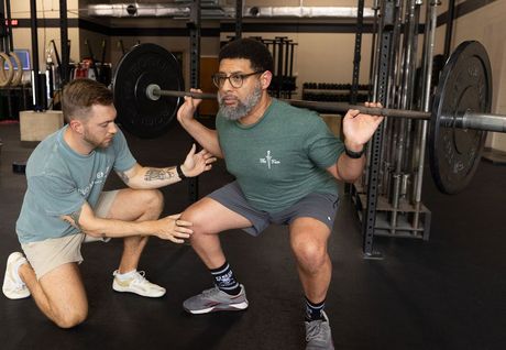 Trainer spotting a lifter doing a barbell squat in a gym