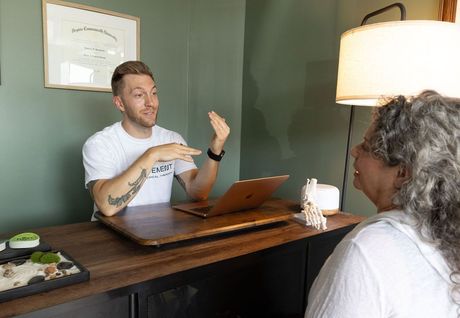 Man speaking at a small table across from a seated woman in a cozy office setting