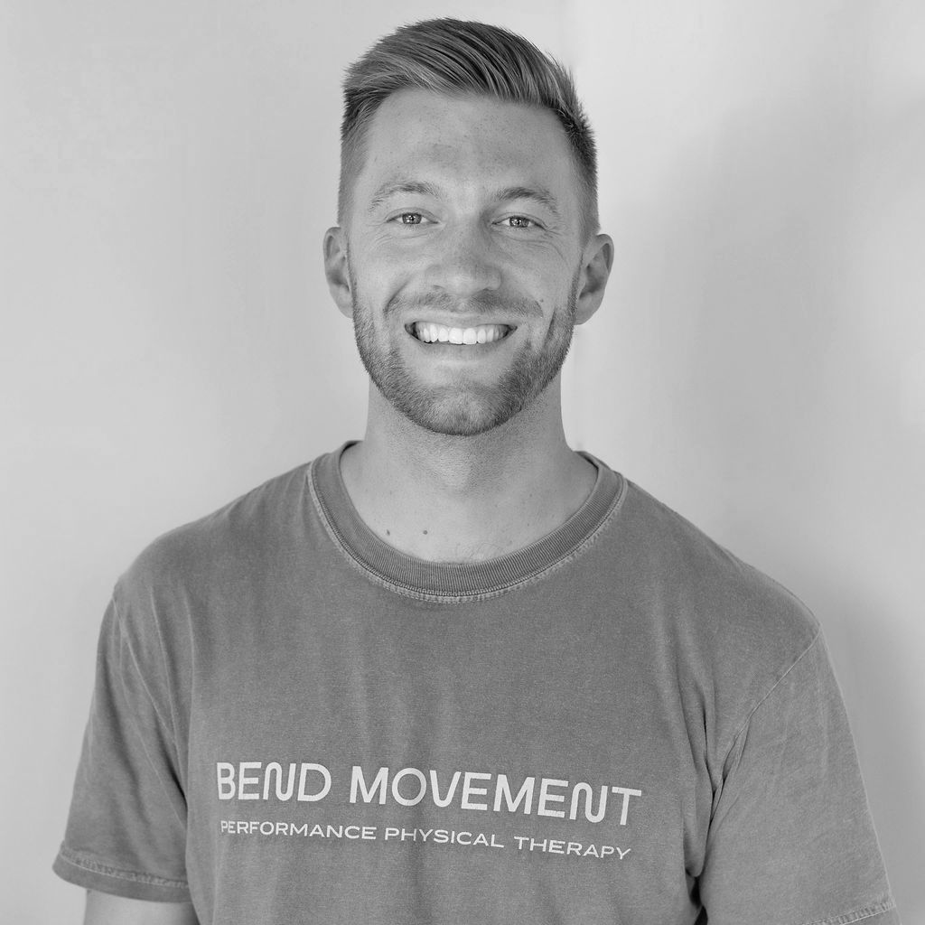 Smiling man in a gray “BEND MOVEMENT” T-shirt against a plain background