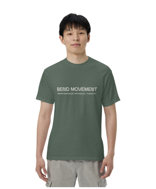 Man wearing a green “BEING MOVEMENT” T-shirt and light pants against a white background