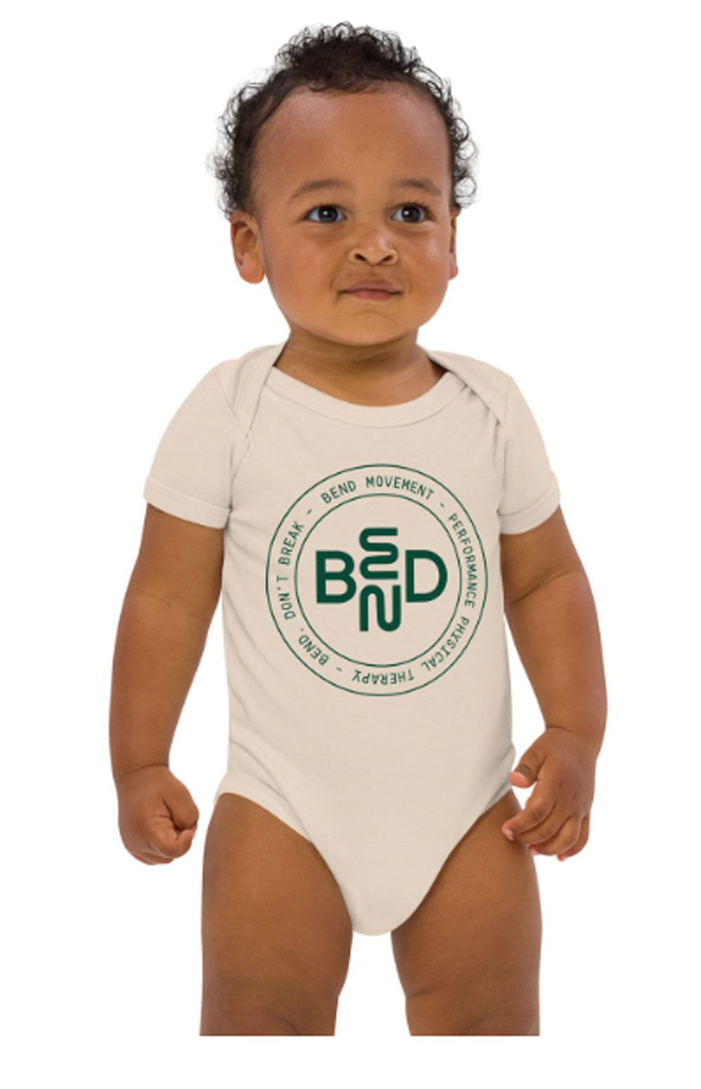 Baby in beige onesie with green logo, standing against a white background