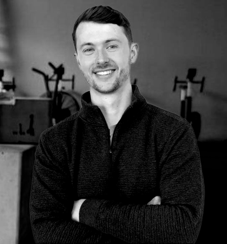 Smiling man in a dark sweater with arms crossed, standing in a gym