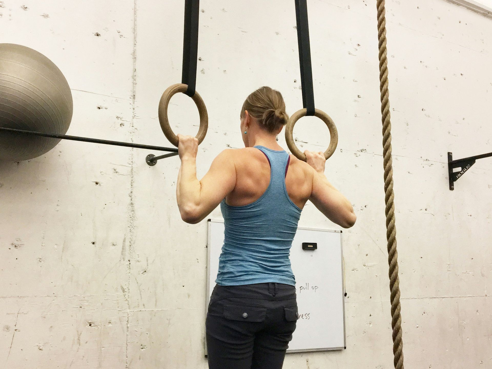 A woman is climbing up gymnastic rings in a gym.