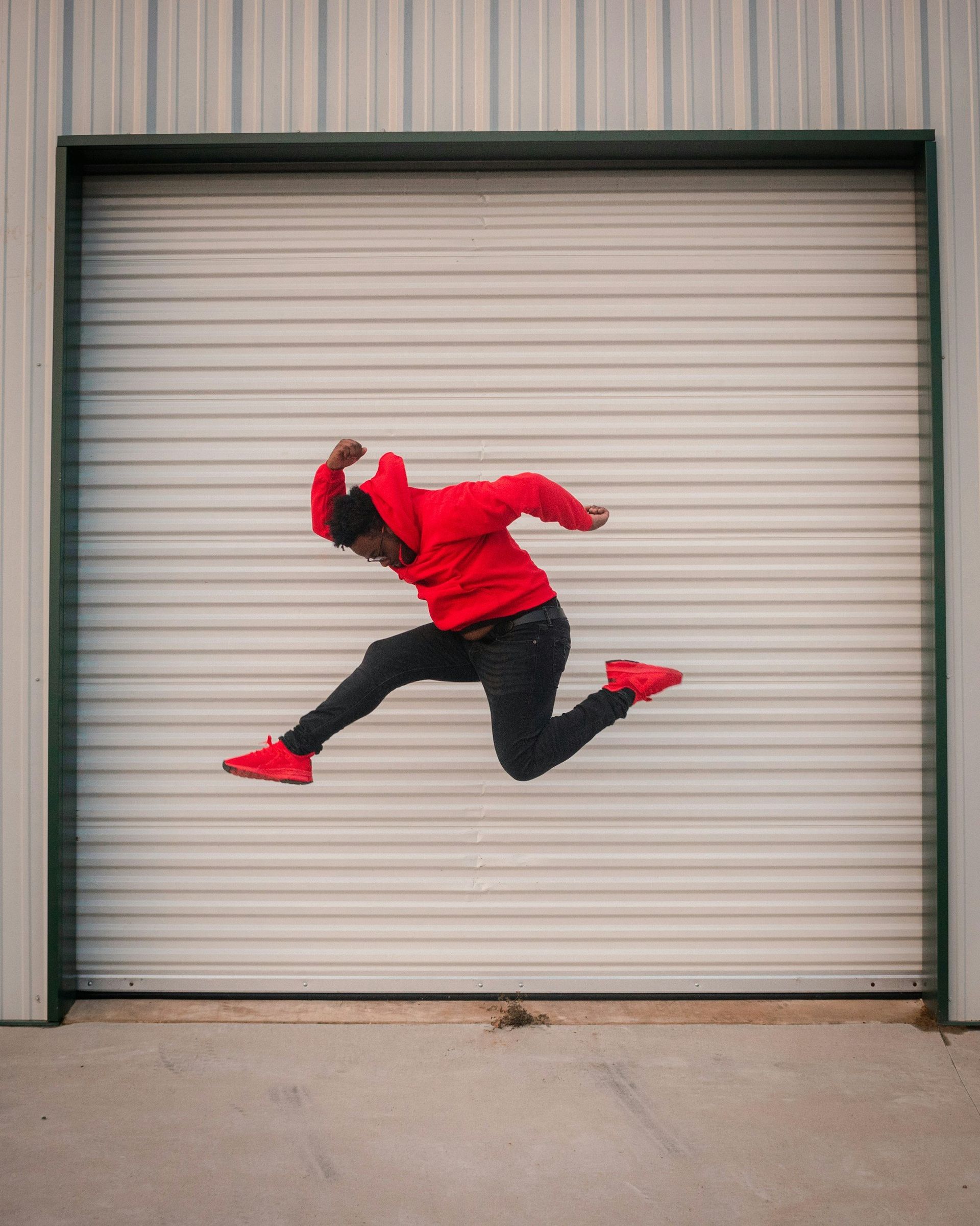 Person in a red jacket and black pants jumping in front of a closed garage door