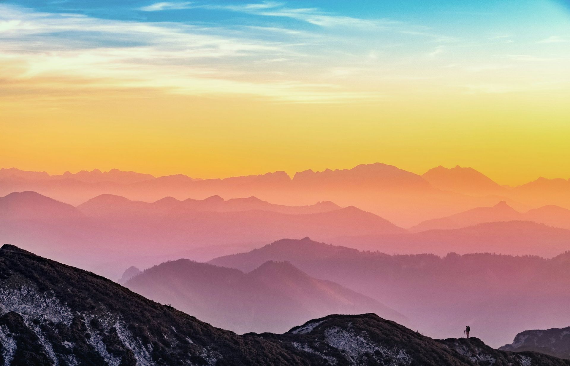 A person is standing on top of a mountain at sunset.