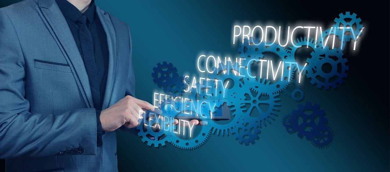 A person in a suit pointing at a digital display of interconnected gears and the words Productivity, Connectivity, Safety.