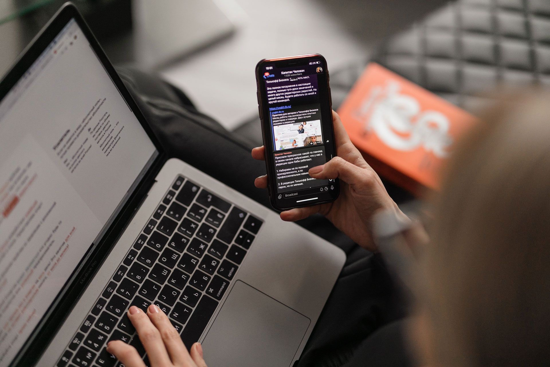 Person using a laptop and a smartphone indoors. Orange box visible.