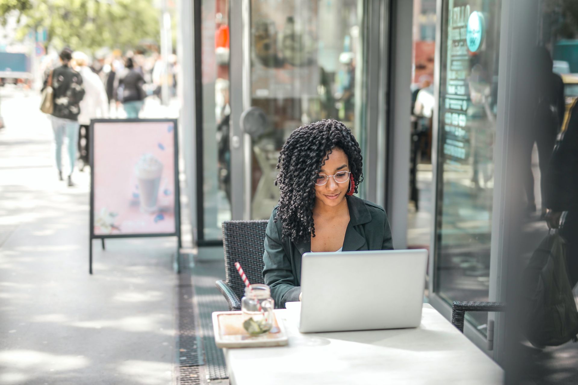 Woman with curly hair works on laptop at outdoor cafe table, sunny day.