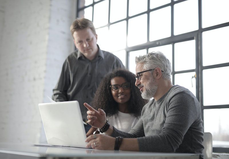Three people looking at laptop screen in an office setting; one points at the screen.