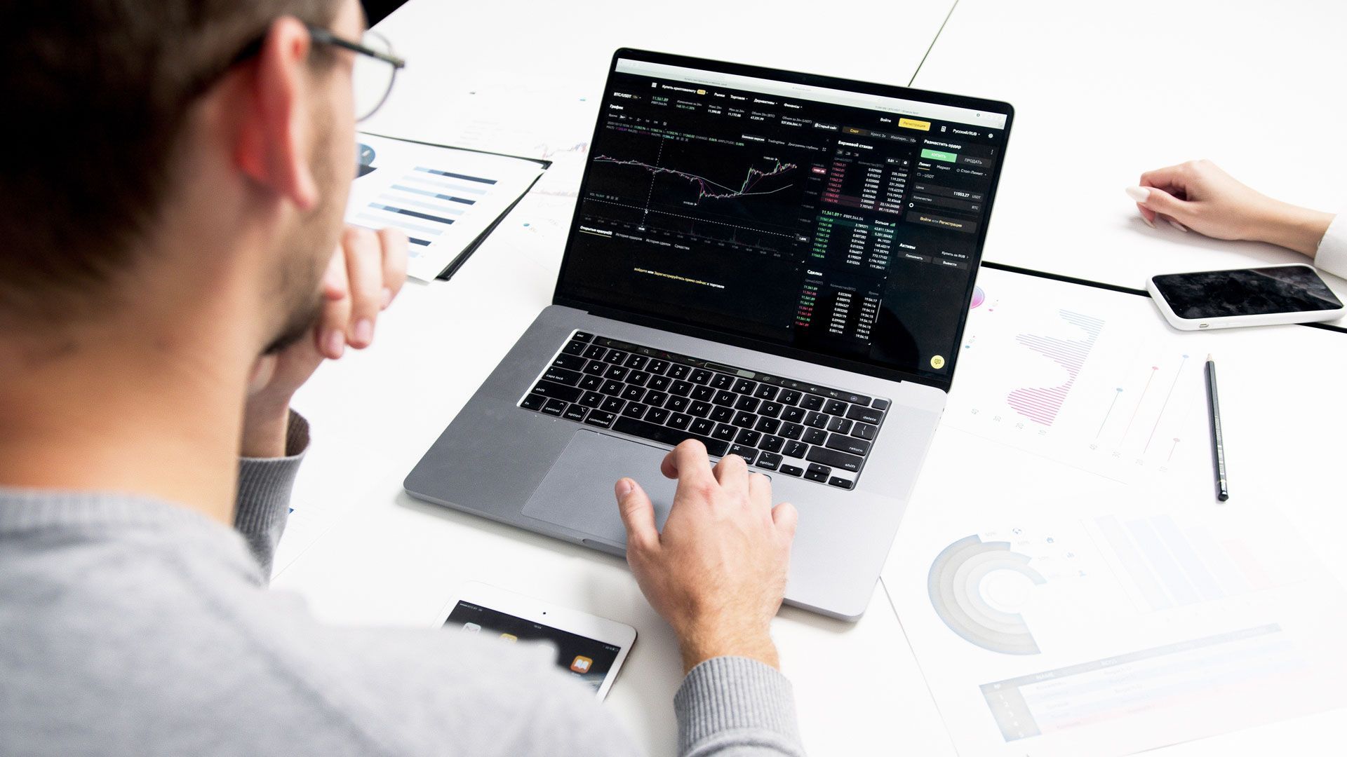 Person using laptop, possibly for financial analysis, with charts and data on screen, sitting at a table.