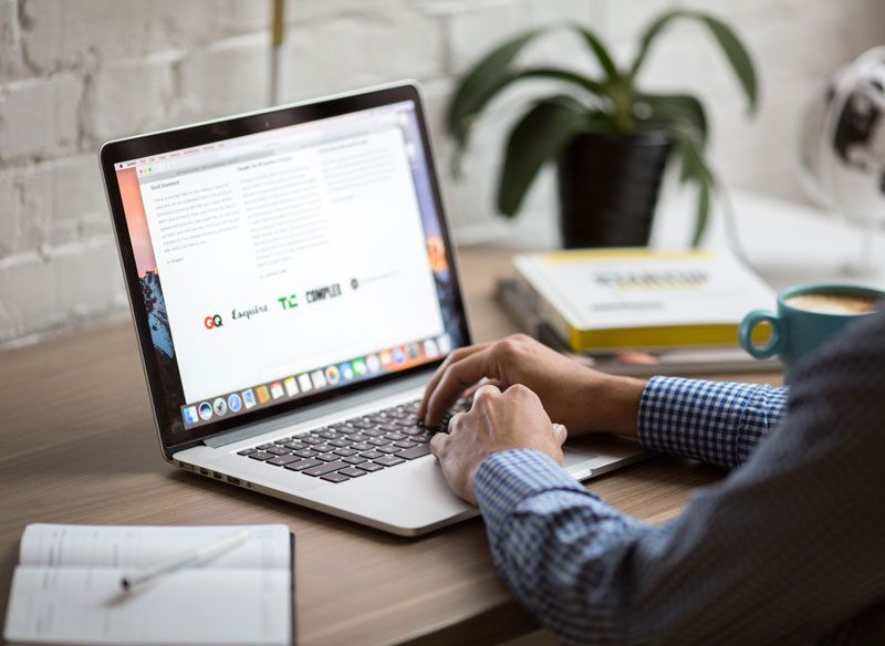Person typing on a laptop at a desk, with a coffee mug and a notebook nearby.