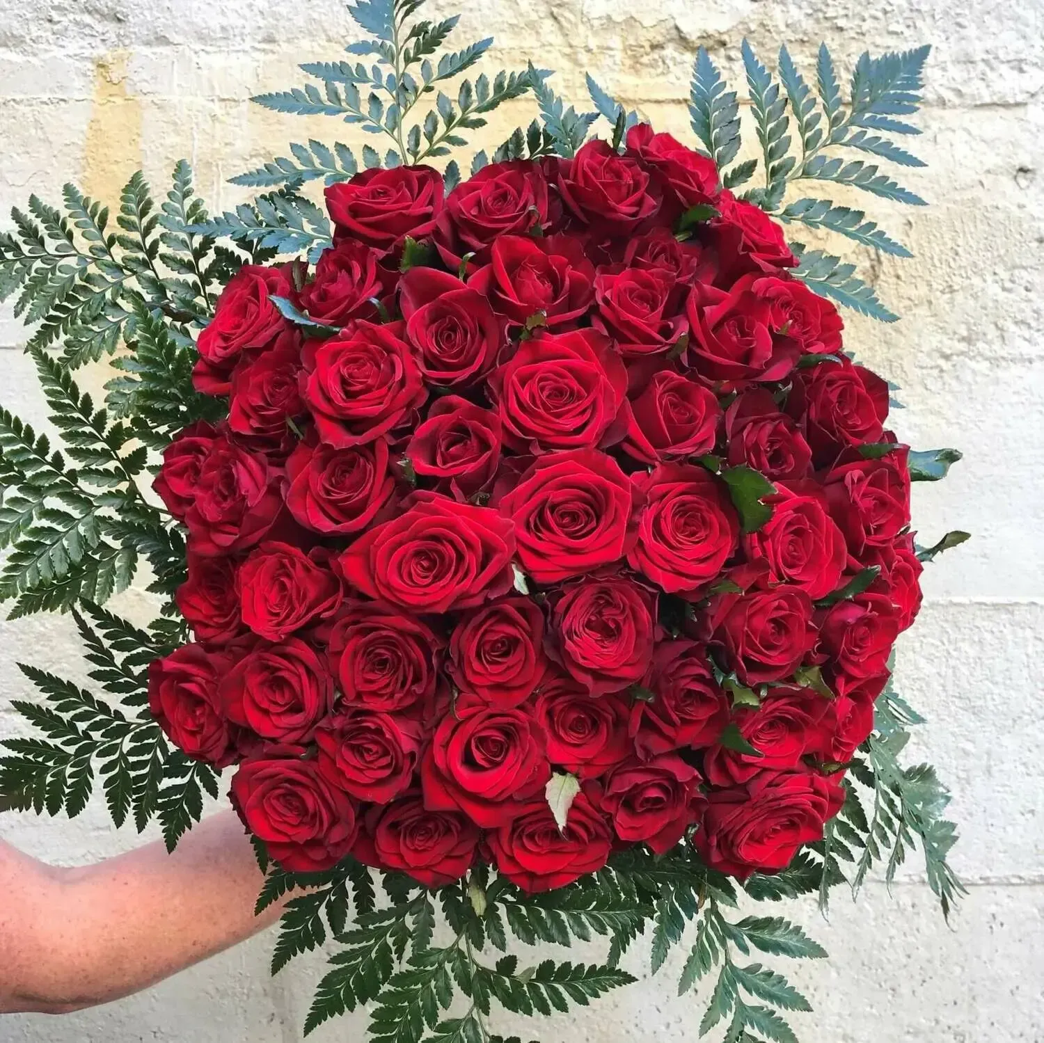 A person is holding a large bouquet of red roses