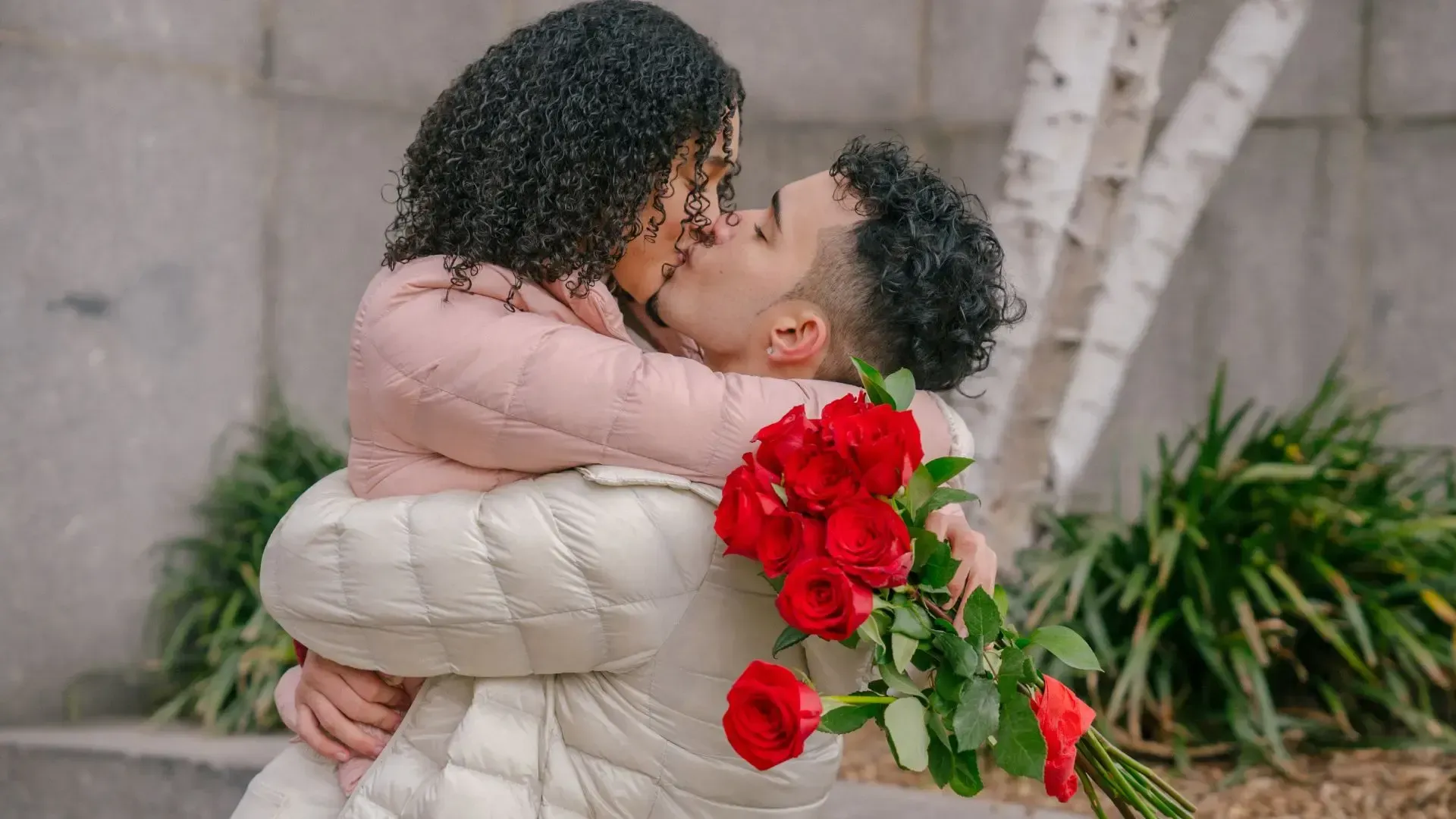 A man is carrying a woman on his shoulders while she holds a bouquet of red roses.