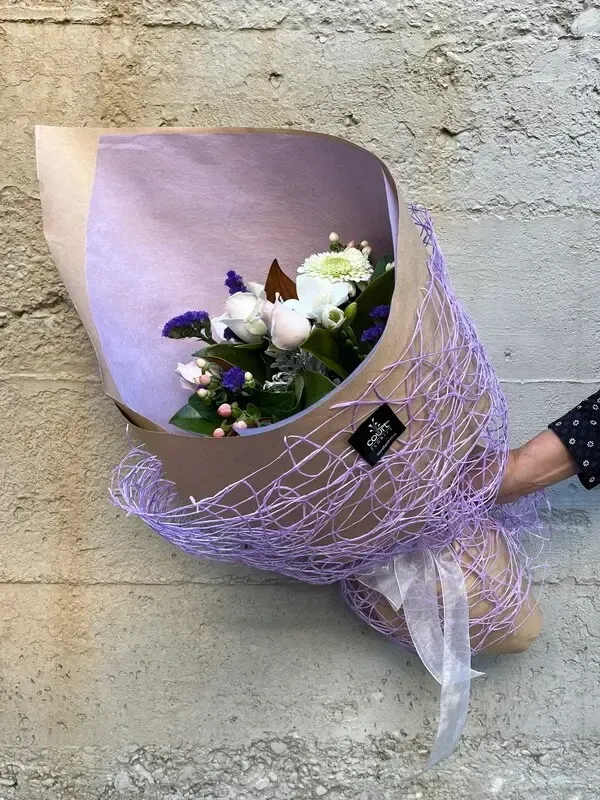 A person is holding a bouquet of flowers wrapped in purple paper.