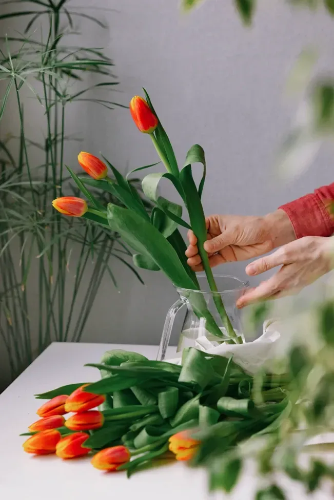 A person is putting flowers in a vase on a table.