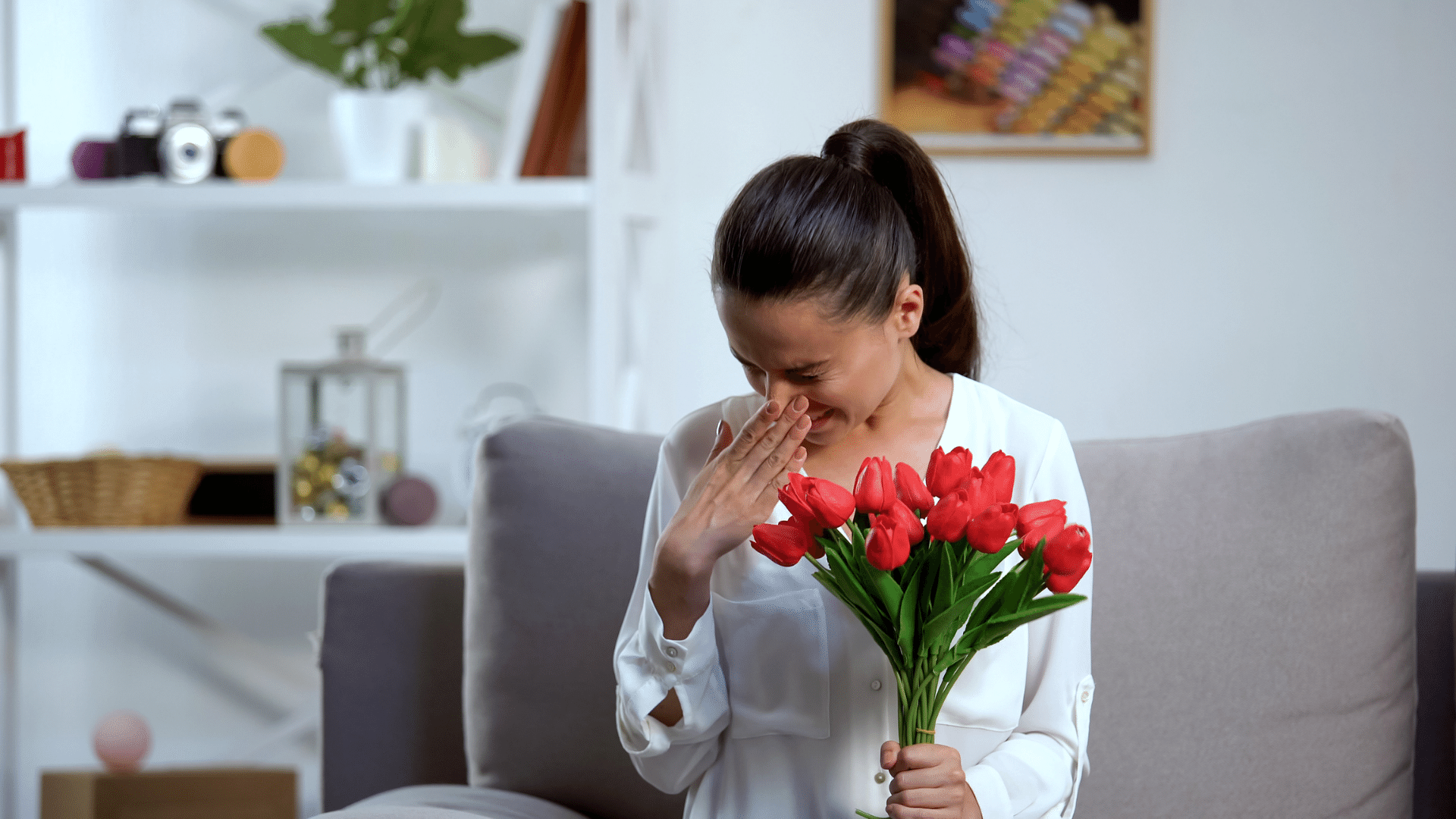 a woman is sitting on a couch holding a bouquet of red flowers .